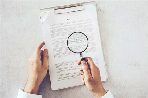 Person holding a magnifying glass over documents