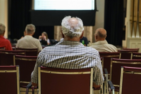 Elderly man sitting in a crowd at a meeting or presentation