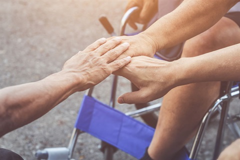 A group of hands placed together in a teamwork motion; wheelchair in background